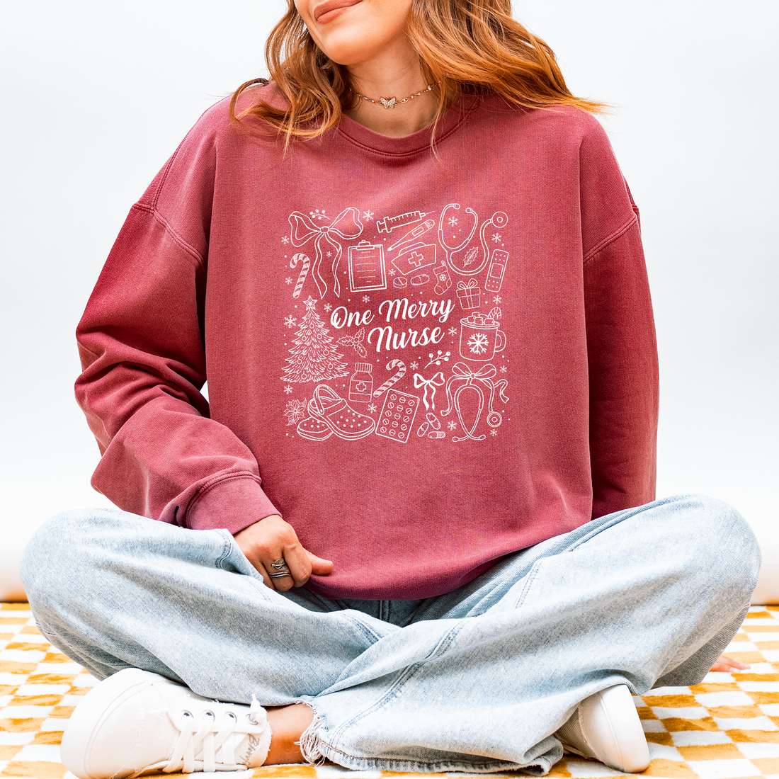 Woman wearing the One Merry Nurse Christmas sweatshirt in Crimson with hand-drawn holiday nurse doodles