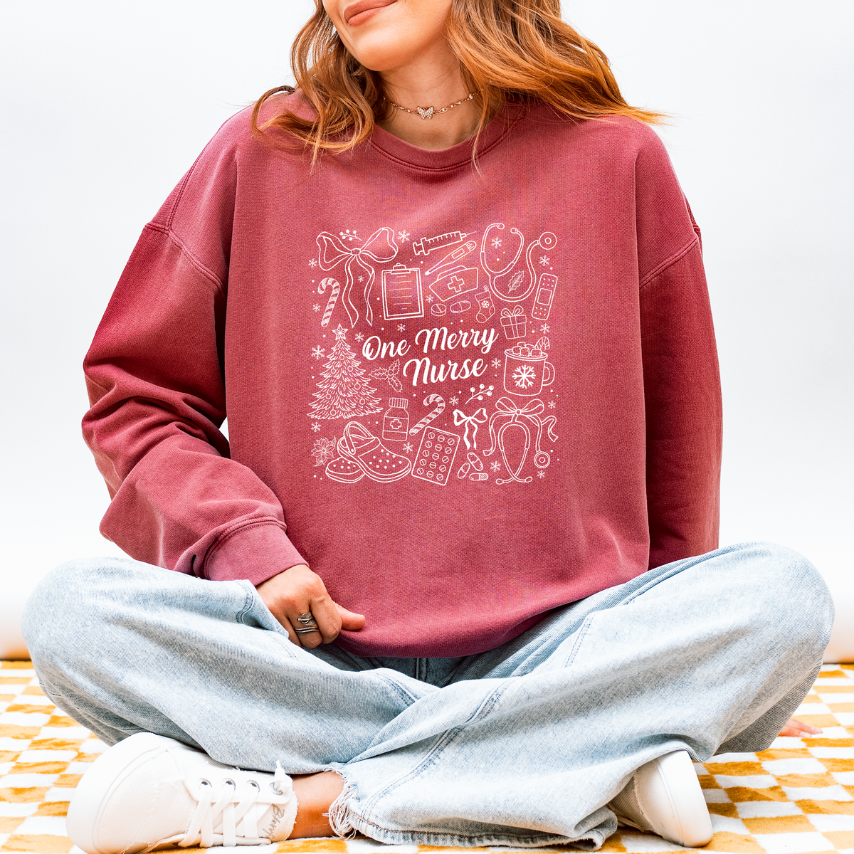Woman wearing the One Merry Nurse Christmas sweatshirt in Crimson with hand-drawn holiday nurse doodles