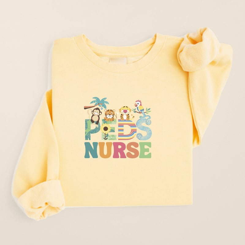 Jungle Friends Peds Nurse Sweatshirt in Butter, folded flat on a warm oat background