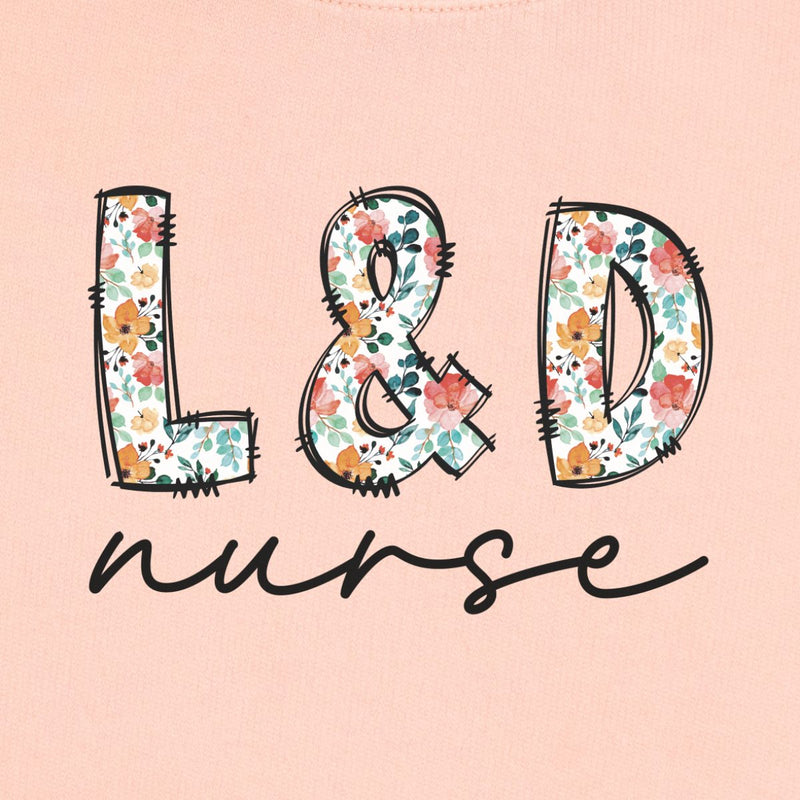 L&D Nurse Floral Sweatshirt in Peachy, close-up of the floral "L&D" letters with black script "nurse" print on a folded crewneck