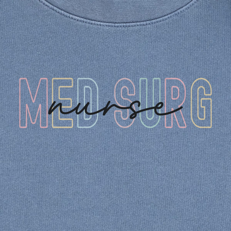 Med Surg Rainbow Nurse Sweatshirt in Blue Jean, close-up of the pastel rainbow "MED SURG" letters with black script "nurse" print on a folded crewneck