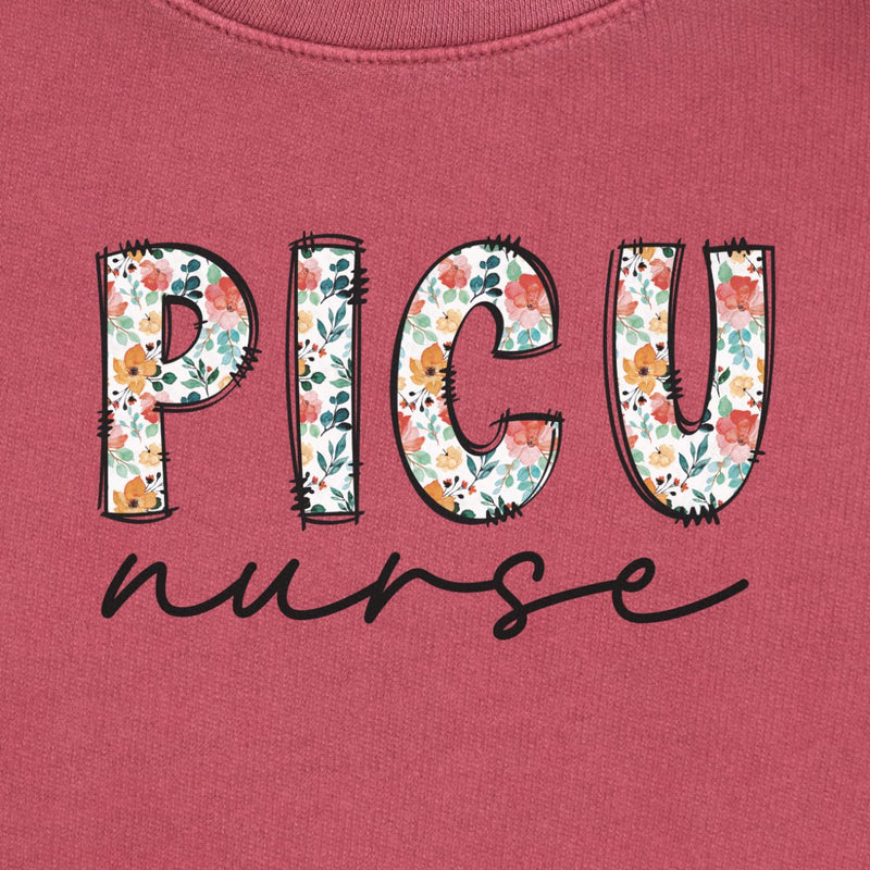 Floral PICU Nurse Sweatshirt in Crimson, close-up of the floral "PICU" letters with black script "nurse" print on a folded crewneck