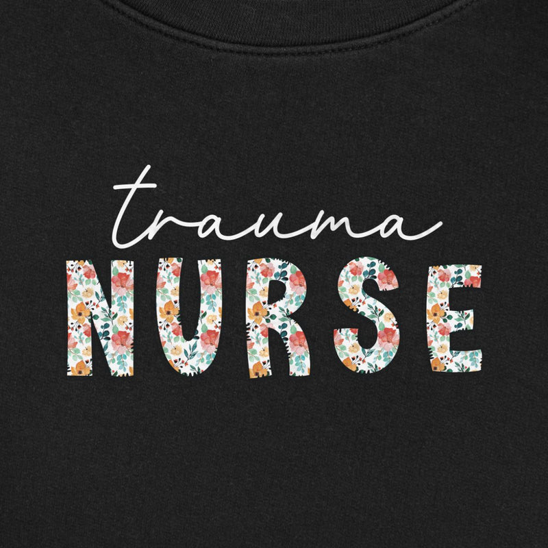Floral Trauma Nurse Sweatshirt (White Script) in Black, close-up of the white script "trauma" over floral "NURSE" letters print on a folded crewneck
