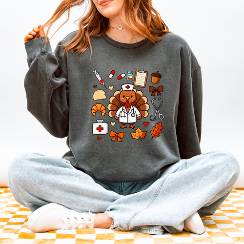 Model wearing Cute Turkey Nurse Thanksgiving sweatshirt in Pepper, front design of turkey nurse in a white coat surrounded by nurse and fall icons, Comfort Colors 1466