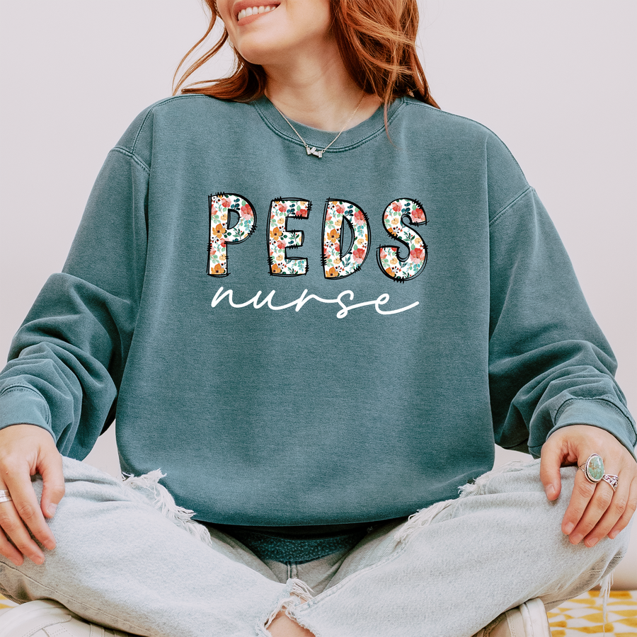 Model wearing the PEDS nurse sweatshirt with floral block letters and white script