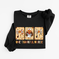 Black One Thankful Nurse Thanksgiving sweatshirt flat lay, One Thankful Nurse lettering with turkey nurse, fall bows and stethoscopes, Comfort Colors 1466