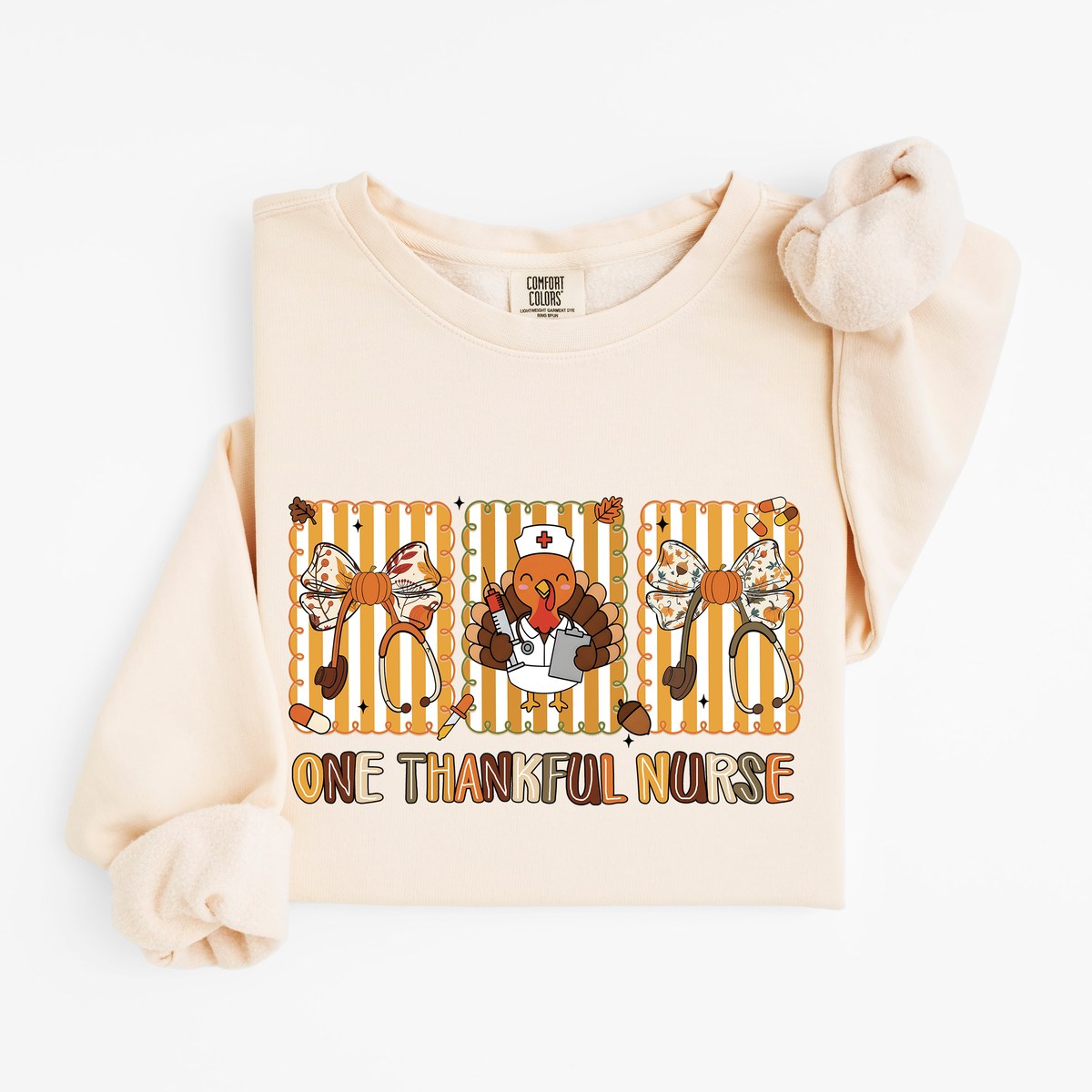 Ivory One Thankful Nurse Thanksgiving sweatshirt flat lay, One Thankful Nurse lettering with turkey nurse, fall bows and stethoscopes, Comfort Colors 1466