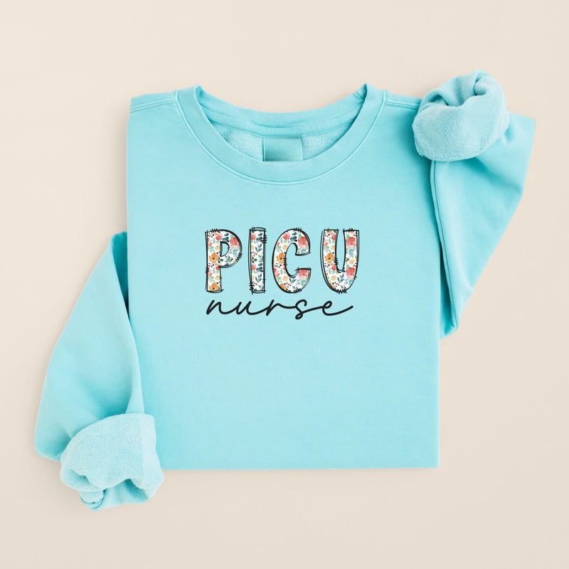 Floral PICU Nurse crewneck in Chalky Mint, folded flat on a warm oat background