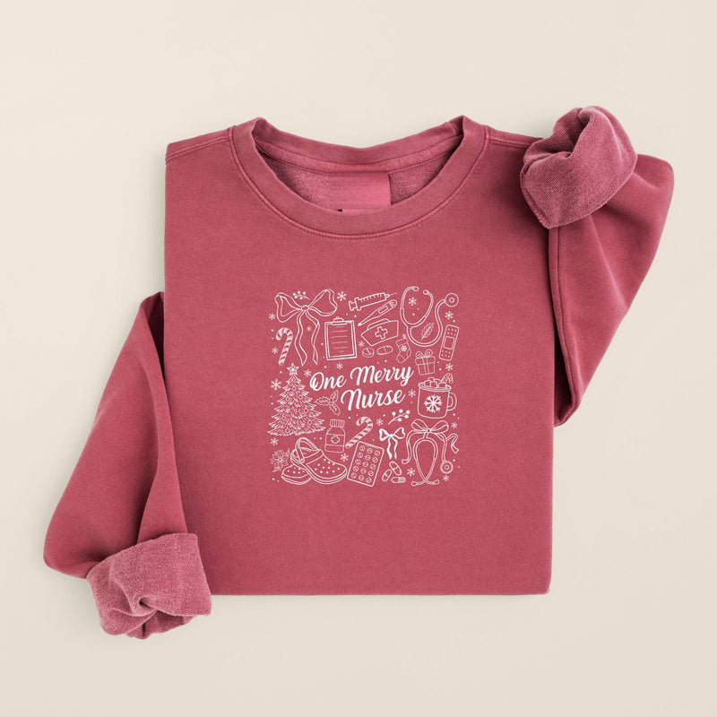 One Merry Nurse Christmas Sweatshirt in Crimson, folded flat on a warm oat background